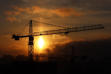 Silhouettes of construction cranes and unfinished residential buildings on sunset background. Housing construction, apartment block in city