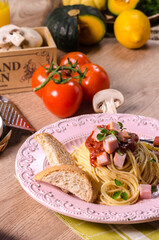 Homemade delicious italian pasta carbonara or spaghetti with ham, garlic, bread, cheese, and tomato sauce marinara in pastel pink dish on green tablecloth on the wooden table.