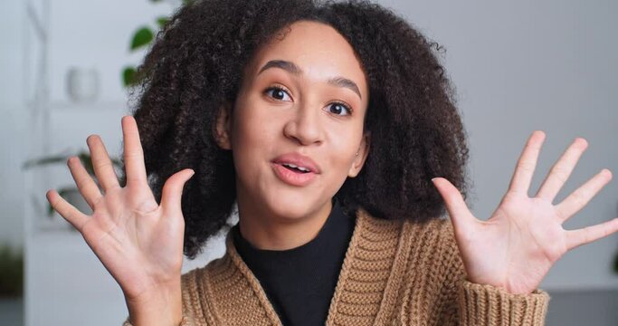 Indoor portrait curly stylish cheerful ethnic teen girl looking at camera smiling counts on fingers one two three shows numbers with her hands first second third imitates explosion of bomb with arms