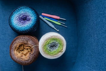 Balls of yarn in different colors and spokes are lying on a blue chair. Top view.