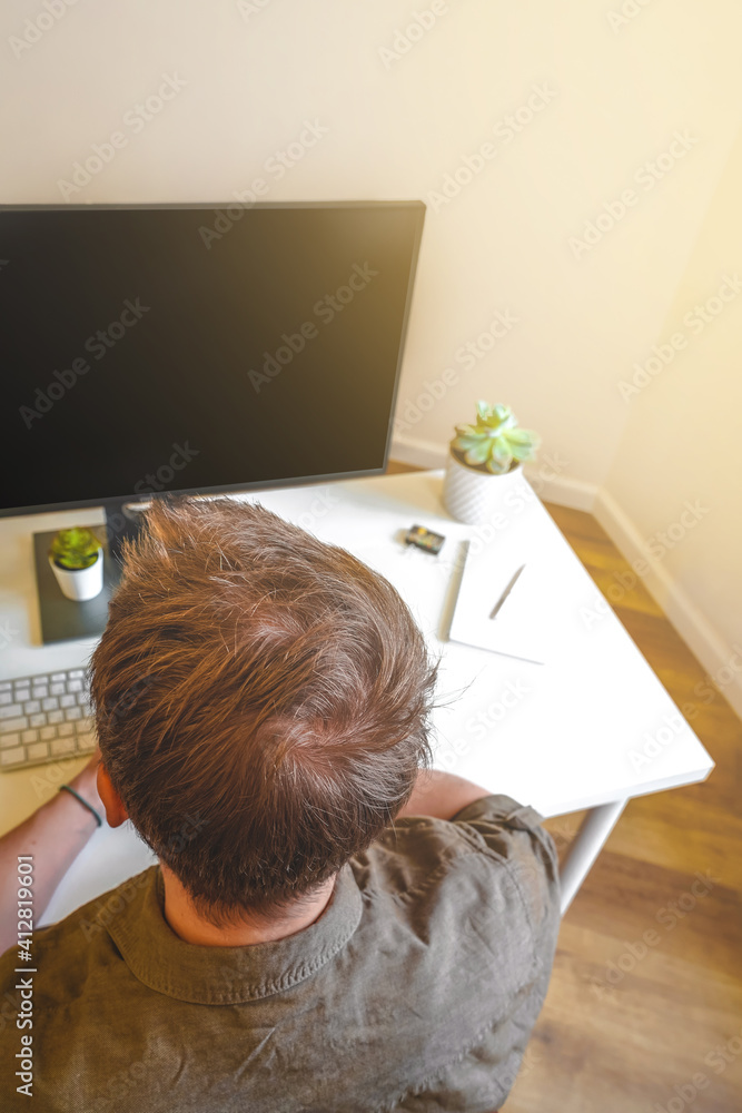 Wall mural a male programmer works in front of a laptop screen in a bright office or remotely from home. workpl
