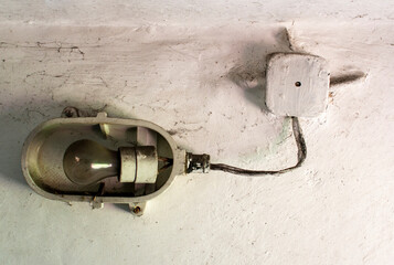 Industrial old ceiling lamp (storage or factory lamp) with vintage off bulb on dirty white wall in a warehouse, basement or attic
