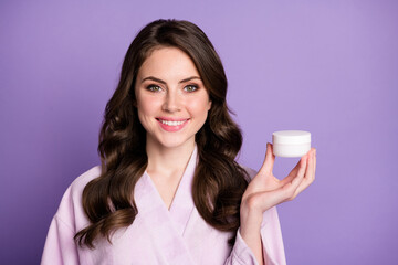 Photo portrait of woman holding cream jar in one hand isolated on vivid violet colored background