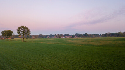 Dramatic and colorful sunrise or sunset sky over a grassy green farmfield shot from drone high up. High quality photo
