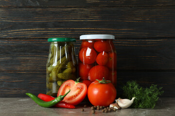 Jars with pickled tomatoes and cucumbers on wooden background