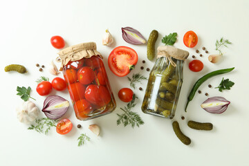 Jars of canned cucumbers and tomatoes, and ingredients on white background
