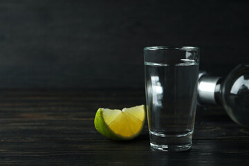 Bottle of vodka, shot and lime slice on wooden background