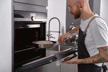 tattooed chef putting proofed rye sourdough bread in cooking pan into oven