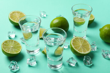 Shots of vodka or tequila, limes and ice on mint background, top view