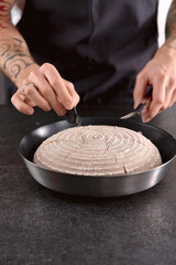 tattooed hands scoring proofed rye sourdough bread in cooking pan
