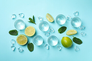 Shots, lime slices, mint and ice cubes on blue background, top view