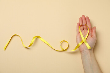 Female hand hold child cancer awareness ribbon on beige background