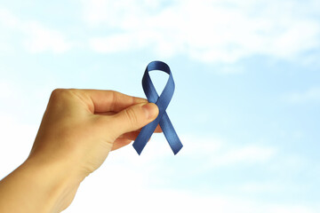 Female hand hold blue awareness ribbon on sky background