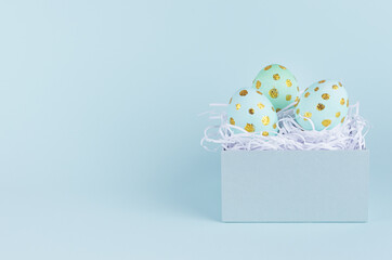 Simple and minimal easter background - easter eggs with golden dots in gift box on blue backdrop.