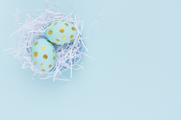 Stylish easter background - blue easter eggs with gold dots in white nest on blue color, top view.
