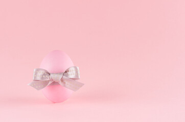 Gentle pink easter egg standing with grey bow on pastel pink background, copy space.