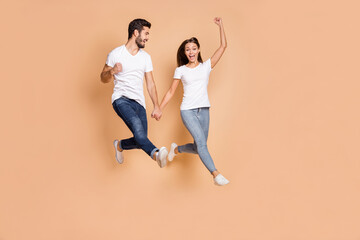 Fototapeta na wymiar Full size photo of young couple happy positive smile jump up celebrate win victory fists hands isolated over beige color background