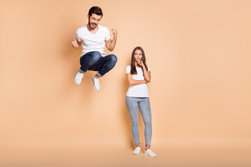 Fototapeta na wymiar Full body photo of young couple he happy jump up rejoice victory she unhappy sad isolated over beige color background