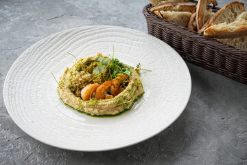 hummus with shrimp and herbs in a white plate on a gray background

