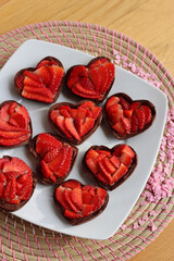 Valentine’s day dessert background. Mini heart shaped chocolate tarts with fresh strawberries on a plate on a wooden table