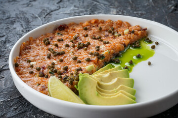 salmon tartare with avacado in a white plate on a dark background close-up
