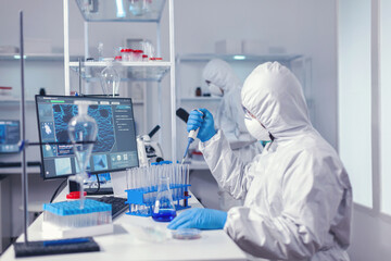 Concentrated scientist using micropipette with a test tube and coworker standing in the background....