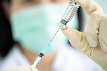 Doctor filling syringe with influenza or COVID vaccine in the clinic. Close up macro of syringe. Woman scientist hand wears medical glove holding vaccine vial. Preparation for injection to the patient