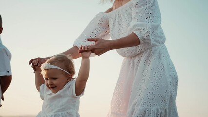 Happy and cheerful family day with dearest people mom, dad, daughter and son. A woman holds small child by handles and girl learns to walk well, and man and boy watch the progress of a small beauty.