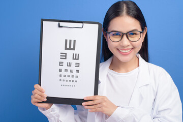 Young female ophthalmologist with glasses holding eye chart over blue background studio, healthcare concept