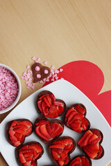 Valentine’s day dessert background. Mini heart shaped chocolate tarts with fresh strawberries and glazed ccokies with sprinkles on a wooden table
