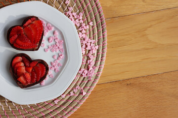 Valentine’s day dessert with copy space. Mini heart shaped chocolate tarts with fresh strawberries on a plate on a wooden table