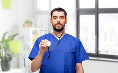 healthcare, profession and medicine concept - doctor or male nurse in blue uniform with stethoscope over medical office at hospital background