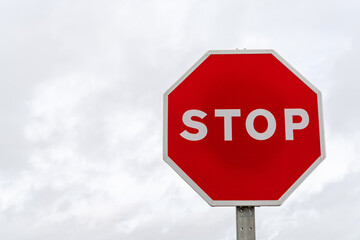 horizontal view of a bright red stop sign with a gray overcast sky behind