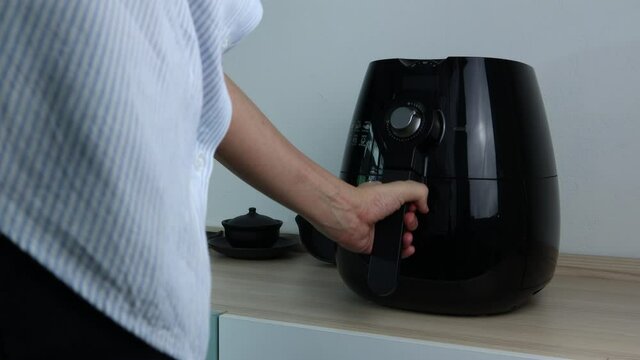 the black air fryer or oil free fryer appliance which is on the wooden table in the white kitchen with white cement wall background for cooking the dinner for family members