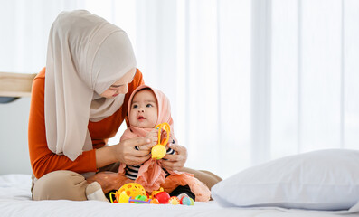 Obraz na płótnie Canvas Beautiful Asian Muslim mather playing with her infant daughter baby in bed room with love and care. There wearing religious hijab dress