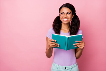 Photo of charming positive dark skin woman look empty space hold book diary isolated on pastel pink...
