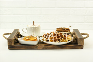 Early breakfast coffee with marshmallows and a stick of cinnamon and Belgian waffles lie on a wooden tray