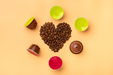 heart shaped coffee beans and capsules around on beige background Top view Flat lay Drink obtained from dosed capsule with roasted, ground and compressed natural coffee