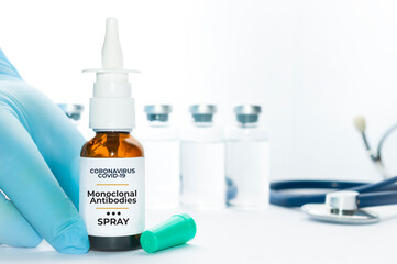 Doctor hold a vial of monoclonal antibodies nasal spray, a new treatment for coronavirus Covid-19, on a white table with some vials and a stethoscope on the background. - obrazy, fototapety, plakaty