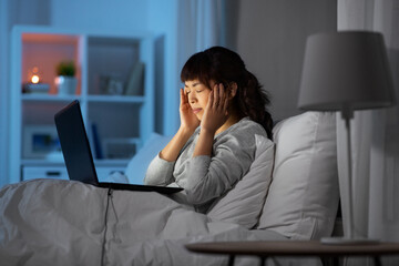technology, remote job and people concept - stressed young asian woman with laptop computer working in bed at home at night