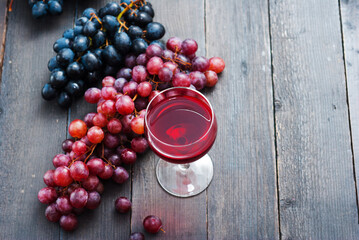 glass of red wine and grapes on black wooden table background