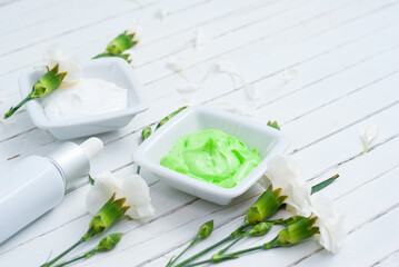 cosmetic creams, perfume in pipette and white flowers on bright wooden