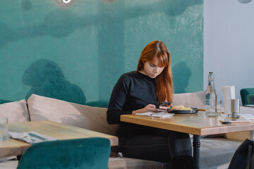 Girl using mobile phone while having lunch in cafe indoors