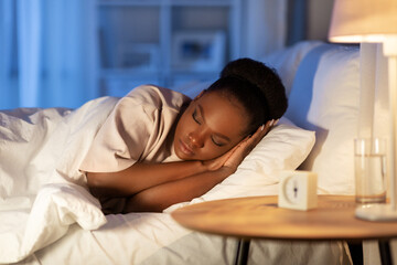 people, relax and comfort concept - young african american woman sleeping in bed at home at night