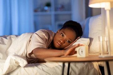 people, bedtime and rest concept - african american woman awaking because of alarm clock at night
