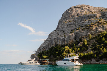 Fototapeta premium White yachts in the black Sea near the shore on the background of a stone cliff and trees