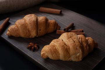Fresh croissants close up on a wooden stand with cinnamon. On a dark background.