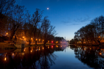 romantic park at night with a lake and water reflection and a fountain in it