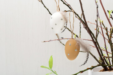 Easter holiday concept with cute handmade white eggs, tree branches, quail feathers and spring flowers on white wooden background.