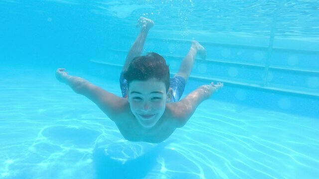 happy boy swimming and dive under blue water in pool